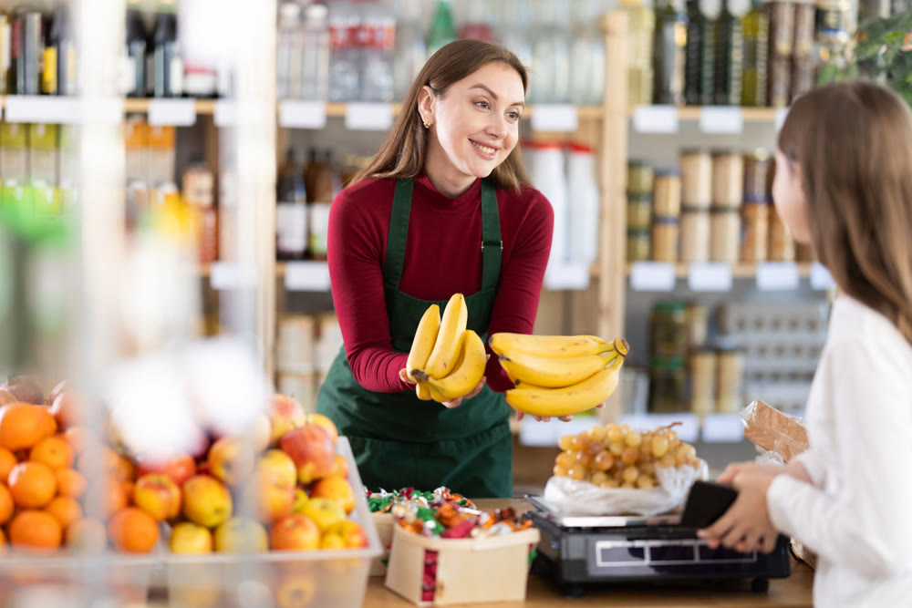 Young saleswoman giving bananas in grocery store