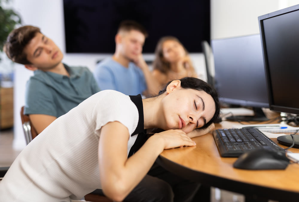 Exhausted girl student sits at table, puts head on crossed arms and sleeps after computer classes