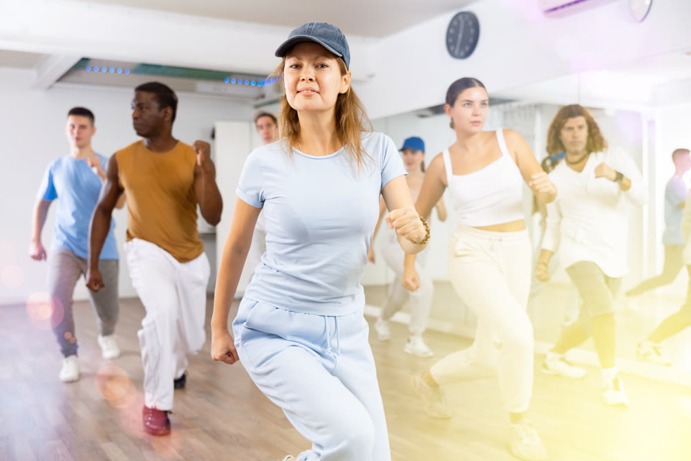 Class of active young adult dancers performing steps during exercising modern dance together in dance hall