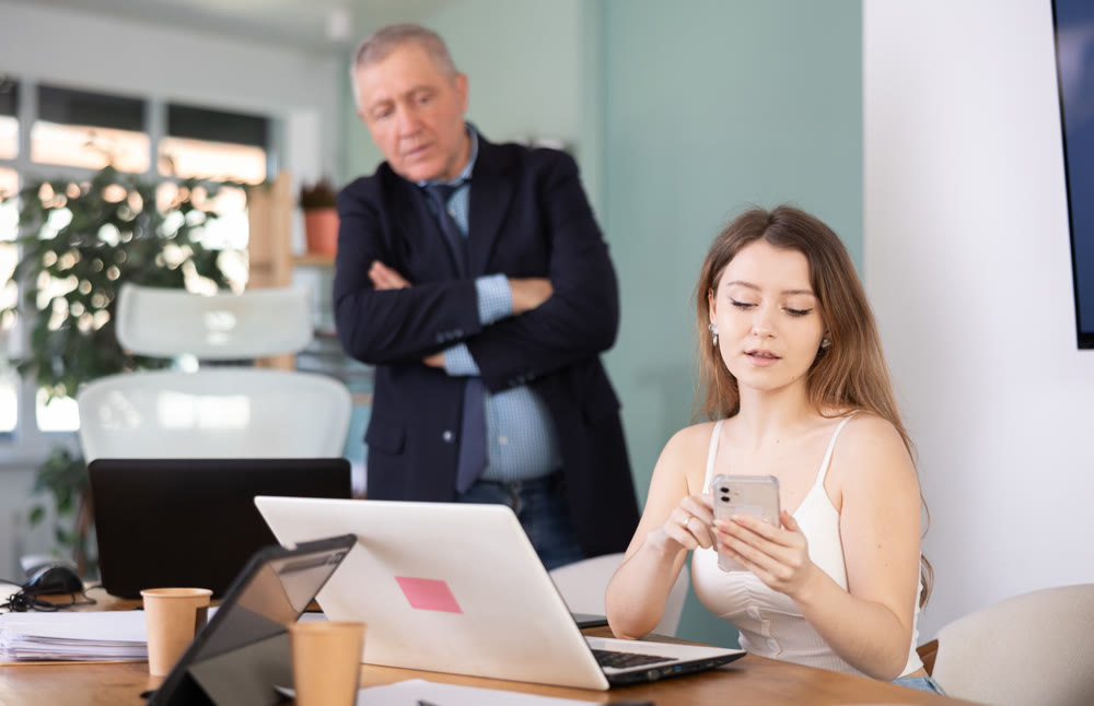 Elderly man scolding young female colleague for sitting with mobile phone