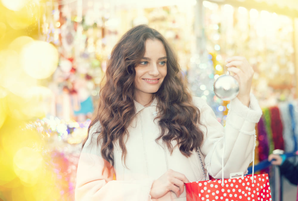Smiling woman with colorful baubles in hands walking on street Christmas fair