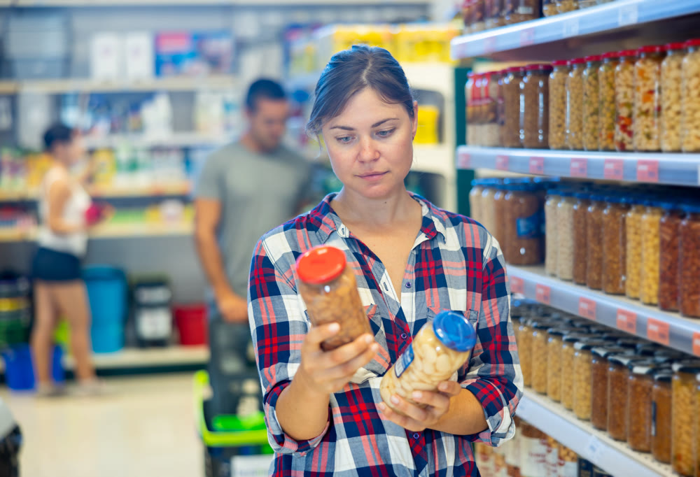 Young woman choosing preserved food in supermarket