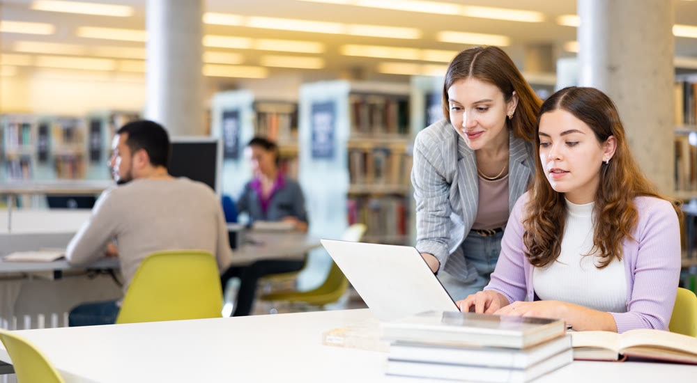 Two young interested women using laptop and books in library