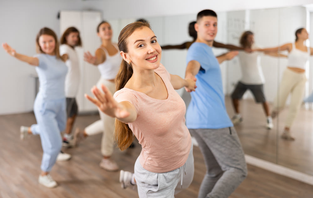 Smiling young adult couples dancing together in pairs and practicing movements in modern choreography class