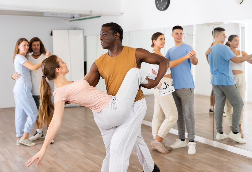 Group of excited young adult people dancing dynamic moves in pairs during lesson in dance class