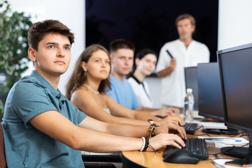Guy with group of students listening to lecture in computer classroom