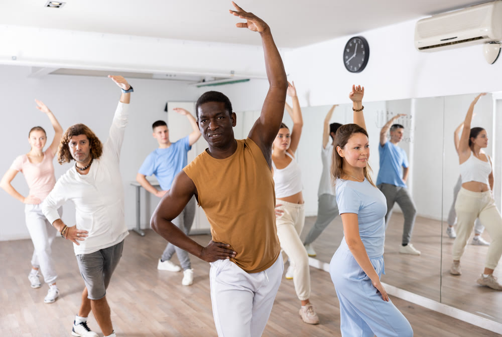 Group of young adult active multiethnic dancers stretching one arm up during learning new dance exercise movement in gym