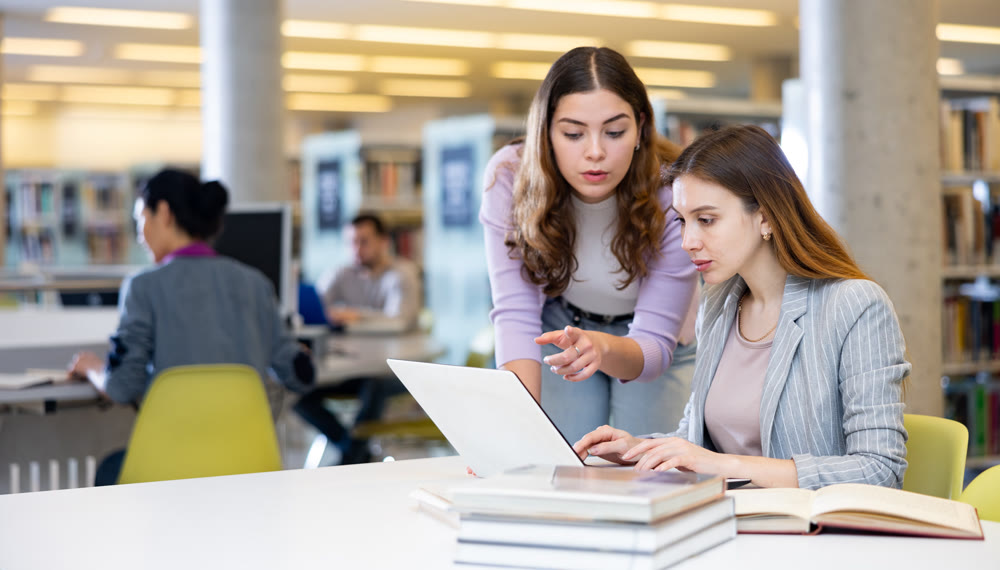 Two women friends studying together at library