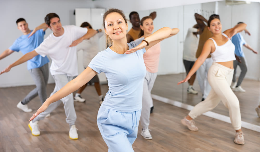 Joyful flexible multiethnic men and women exercising active moves with group of people in dance center