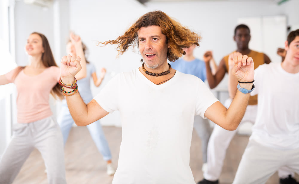 Cheerful energetic multiracial dancers of different ages dancing aerobics at lesson in modern class of gym