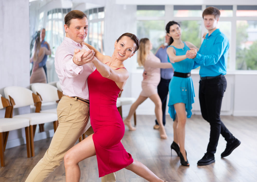 Brunette in red and smiling man enjoying tango in dance studio