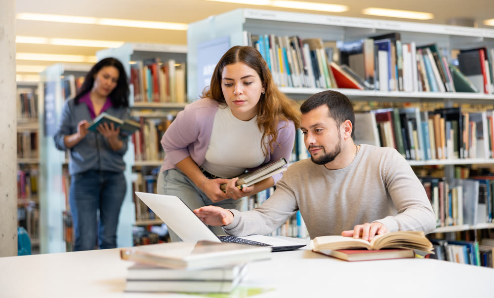 Male and female students preparing for exam together in library
