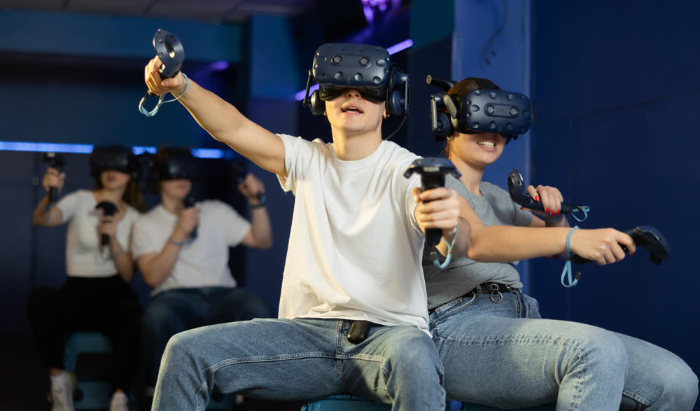 Emotional young couple with VR headsets and joysticks immersed in game