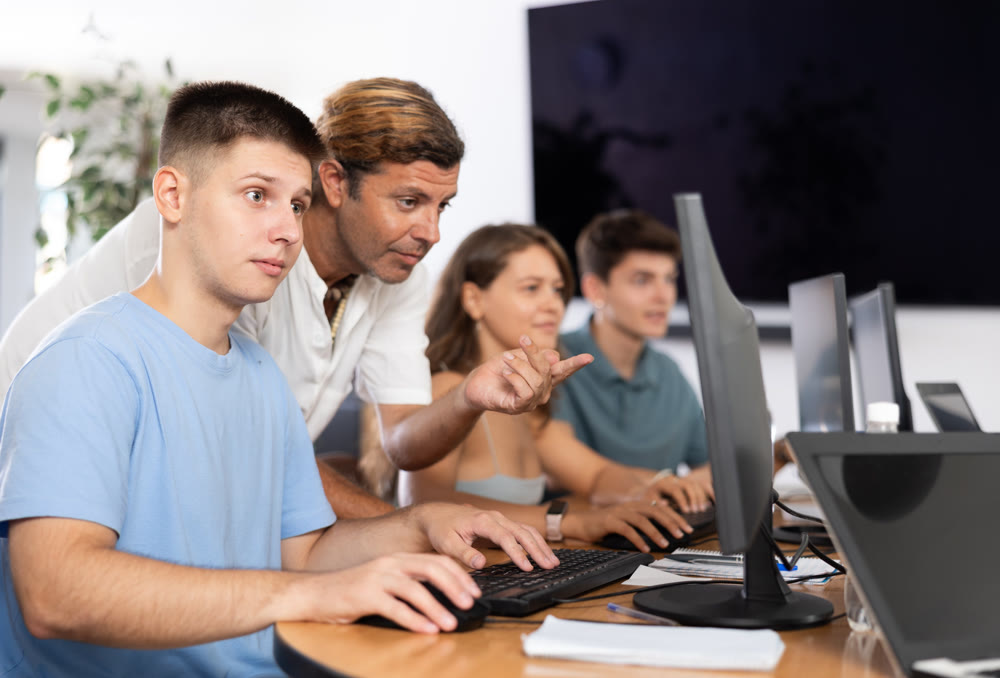 During computer lesson, male teacher helps guy student complete difficult task,