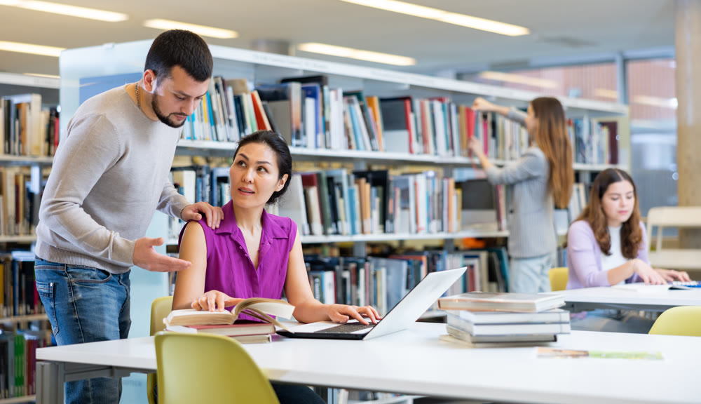 Man and woman working with books and laptop in library