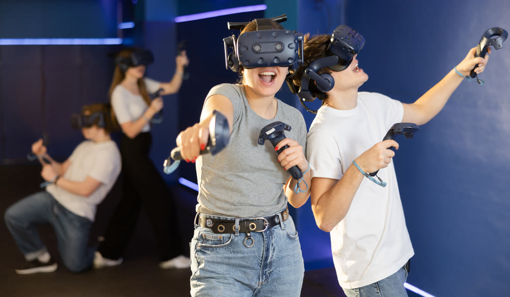 Emotional young couple with VR headsets and joysticks immersed in game