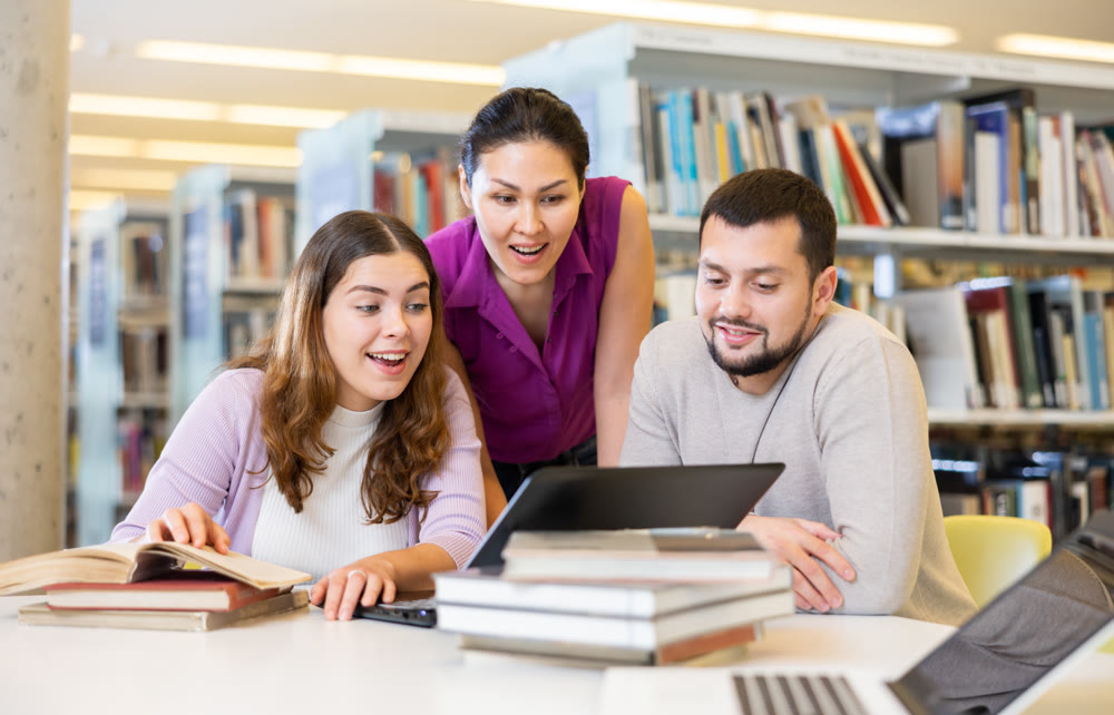 Group of students in the library is preparing for classes on a laptop