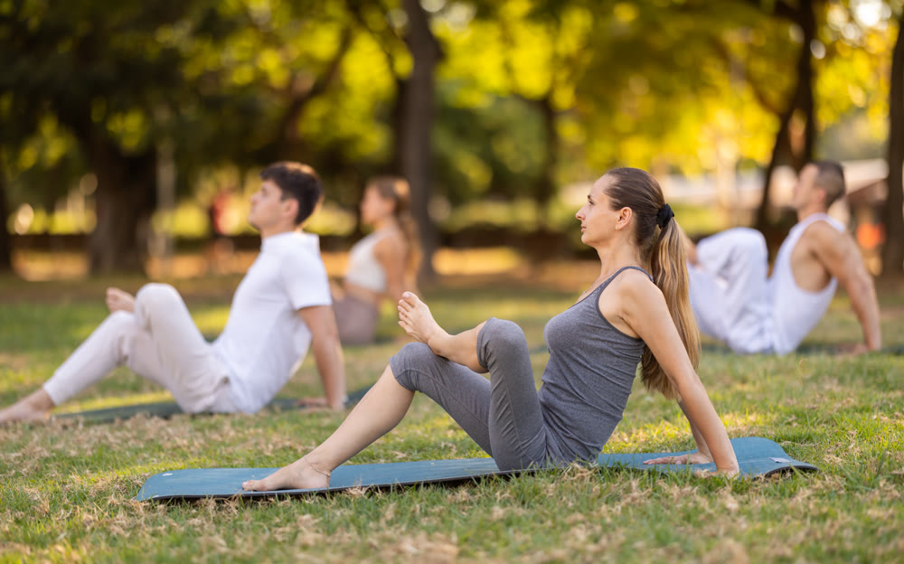 Yoga lesson visitors with girl coach perform halasana in park