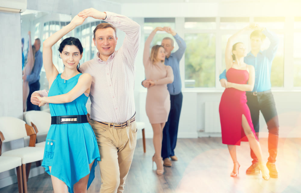 Positive man dancing playful Latin dance bachata with female partner during group class in studio