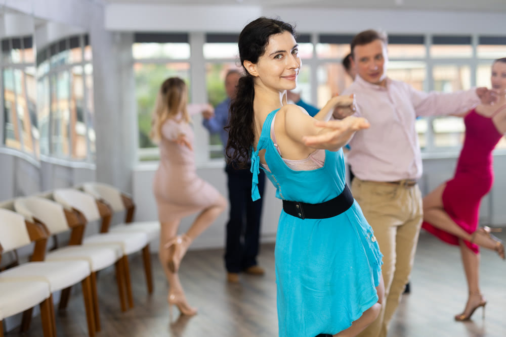 Positive men and women in party clothes enjoying jive in dance studio