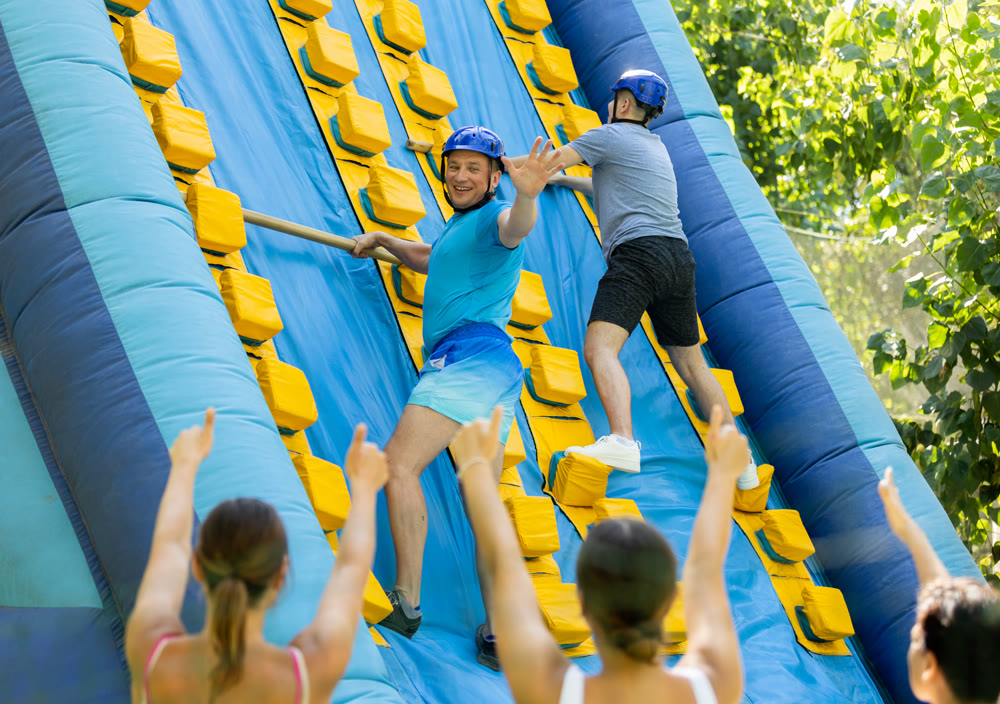 Men using sticks to reach top of slide in adventure park
