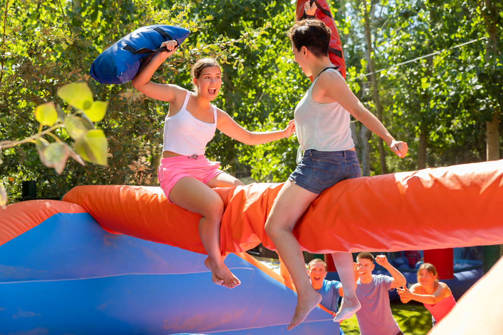 Happy girl funny pillow fighting on inflatable log with female friend
