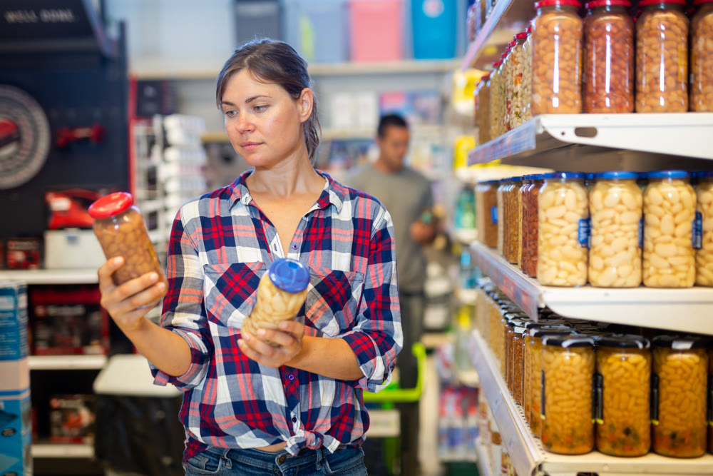 Young woman choosing canned beans in glass jar in supermarket