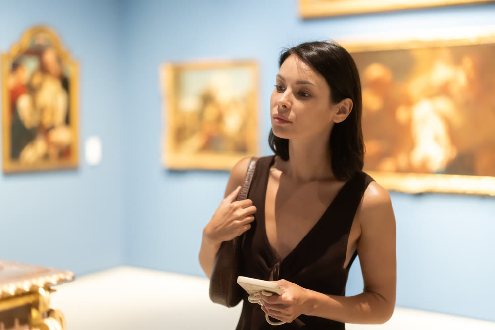 Woman visiting museum and looking at paintings in gold frames