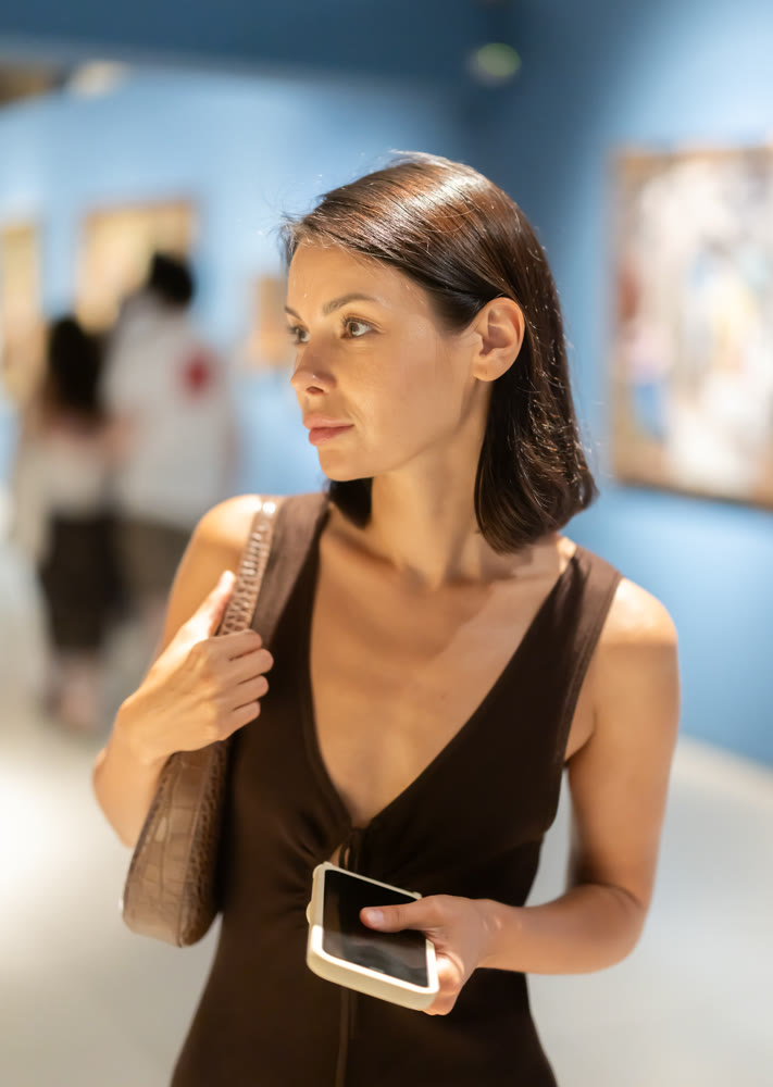 Young woman in summer clothes looking at paintings in museum