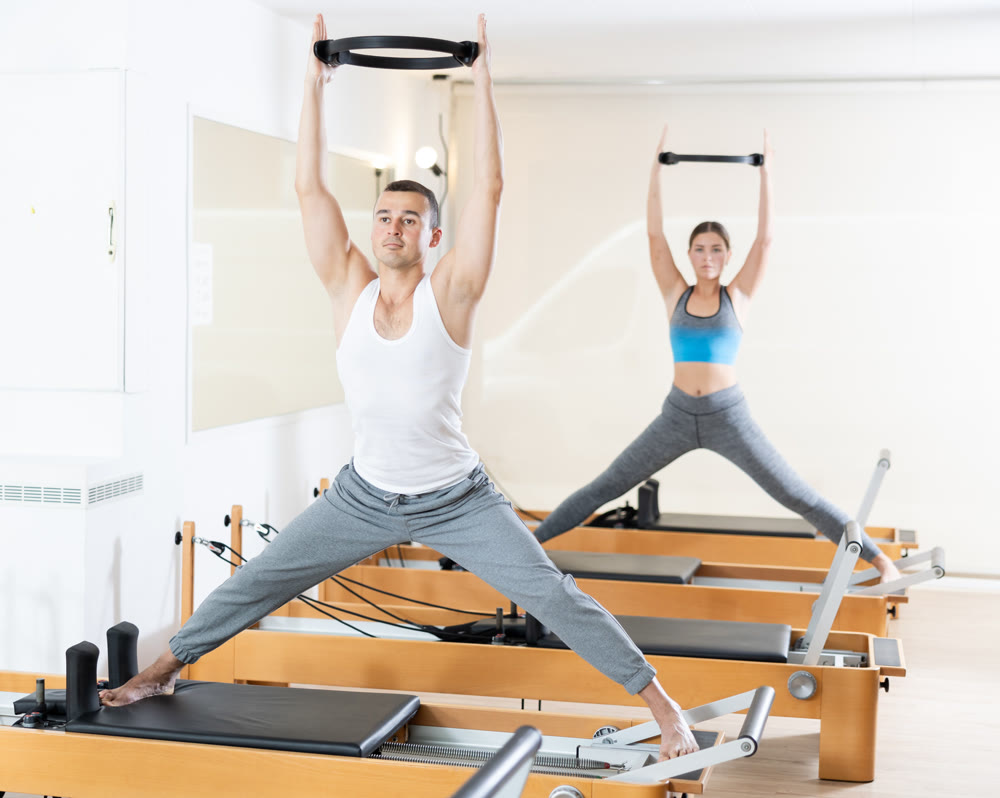 Girl and man exercising with pilates rings on reformer in fitness studio. Healthy lifestyle concept