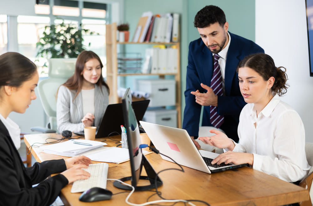 Young man helping female colleague work on laptop
