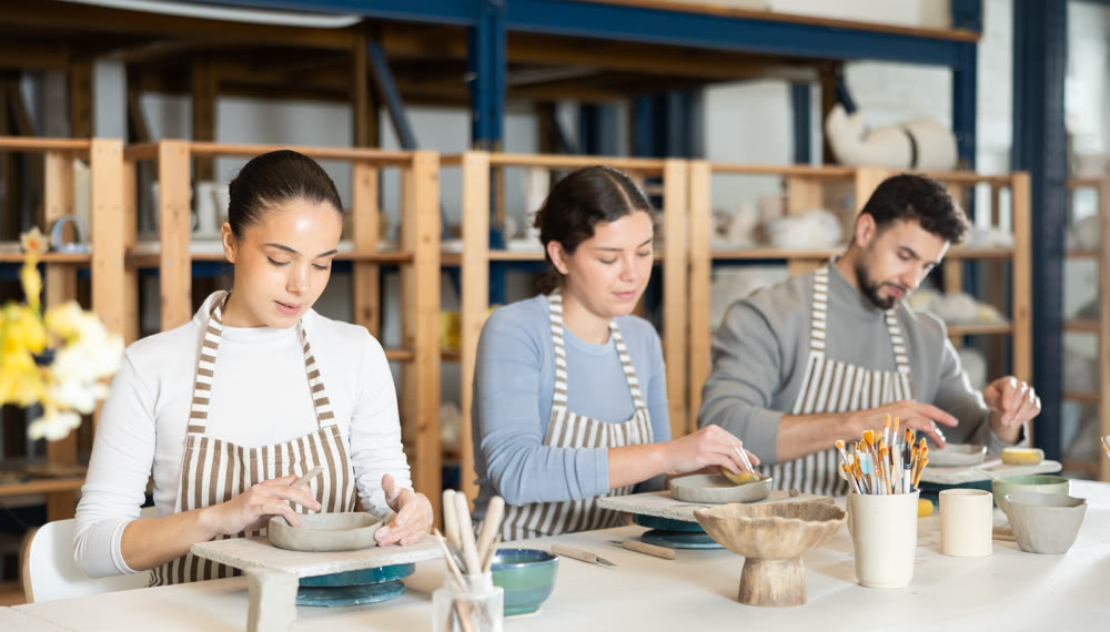 Three pottery workshop workers sculpt from raw clay