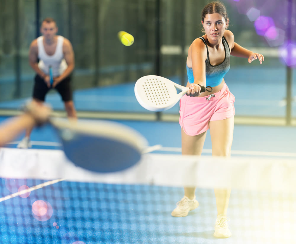 Girl paired with a man plays padel on an indoor tennis court