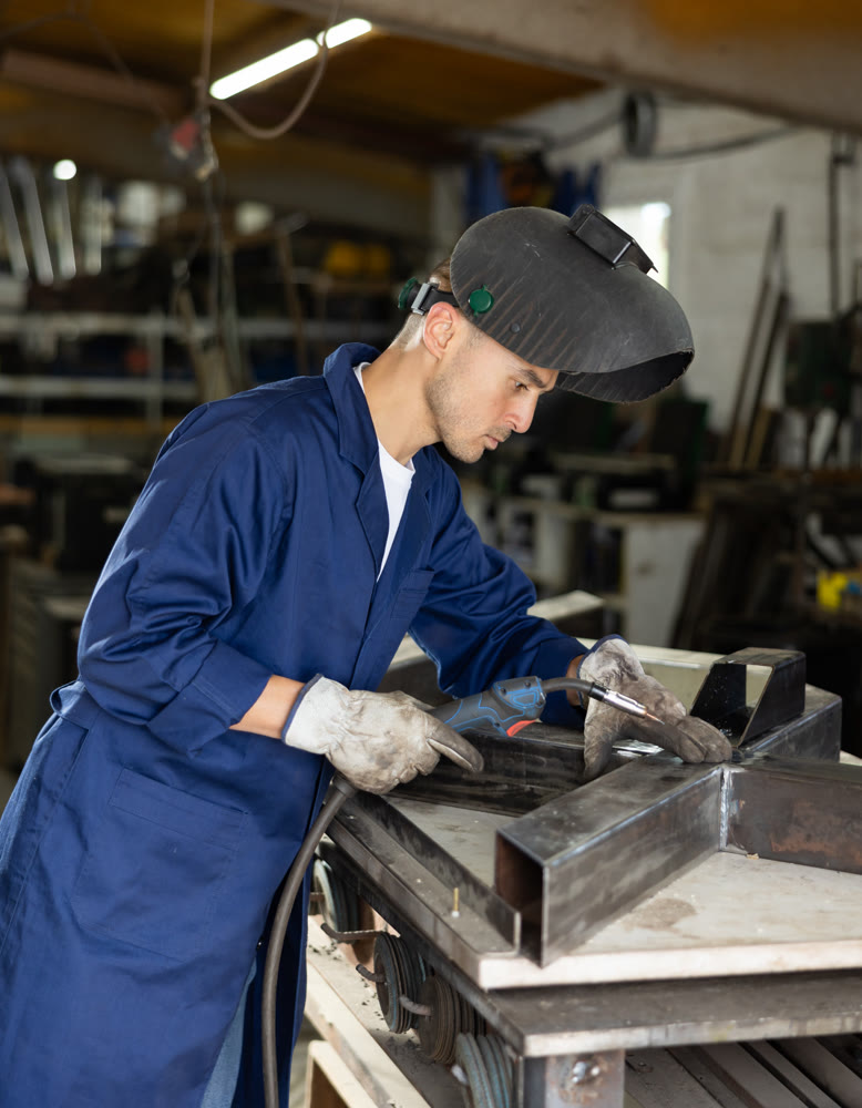 Male welder standing with a welding semi-automatic machine and a safety helmet in metal machining workshop