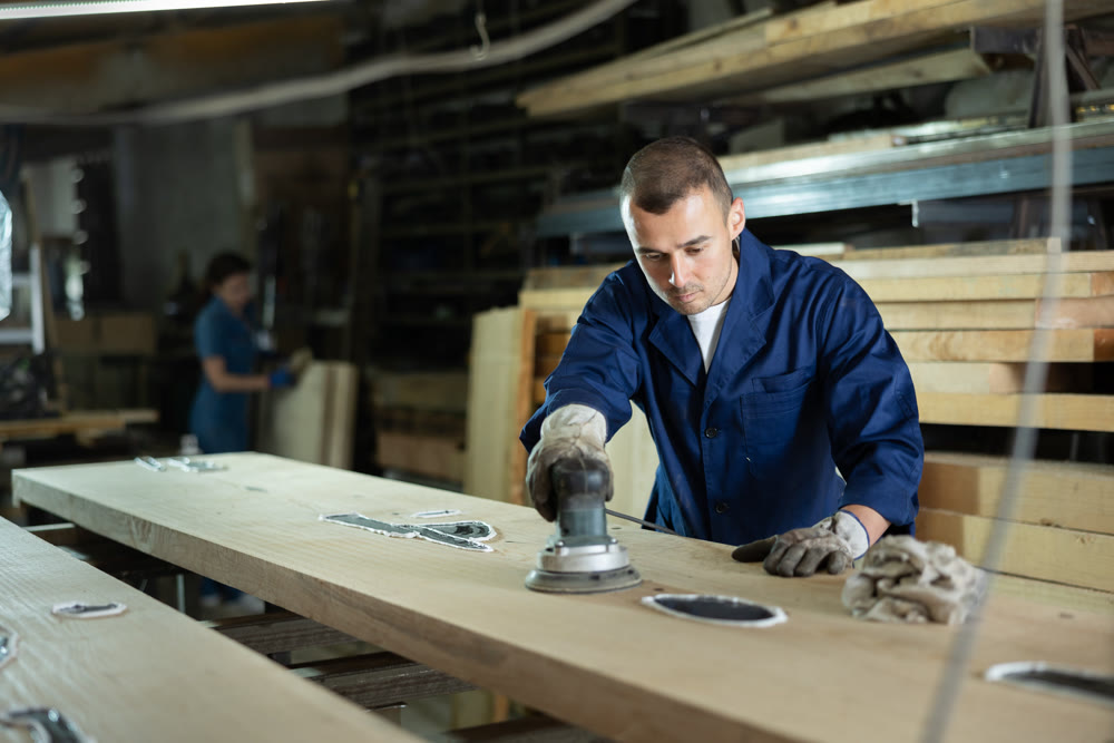 During manufacturing, man employee grinds surface of wooden board, gives smoothness to surface