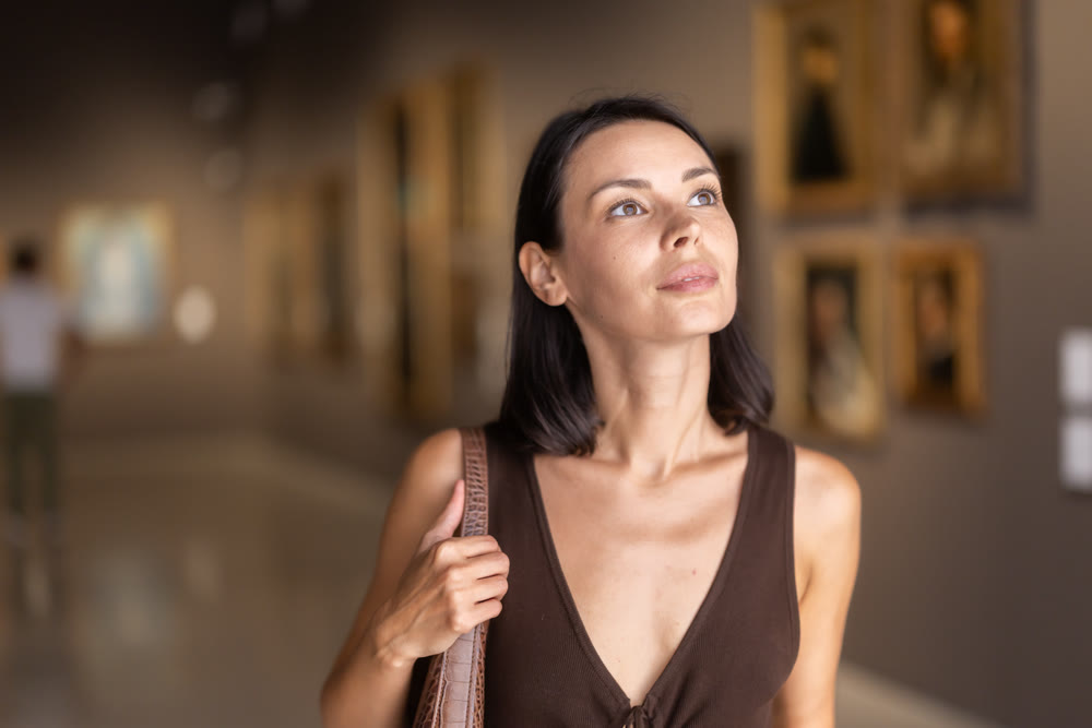 Woman with phone in hands in museum hall, view painting exhibition