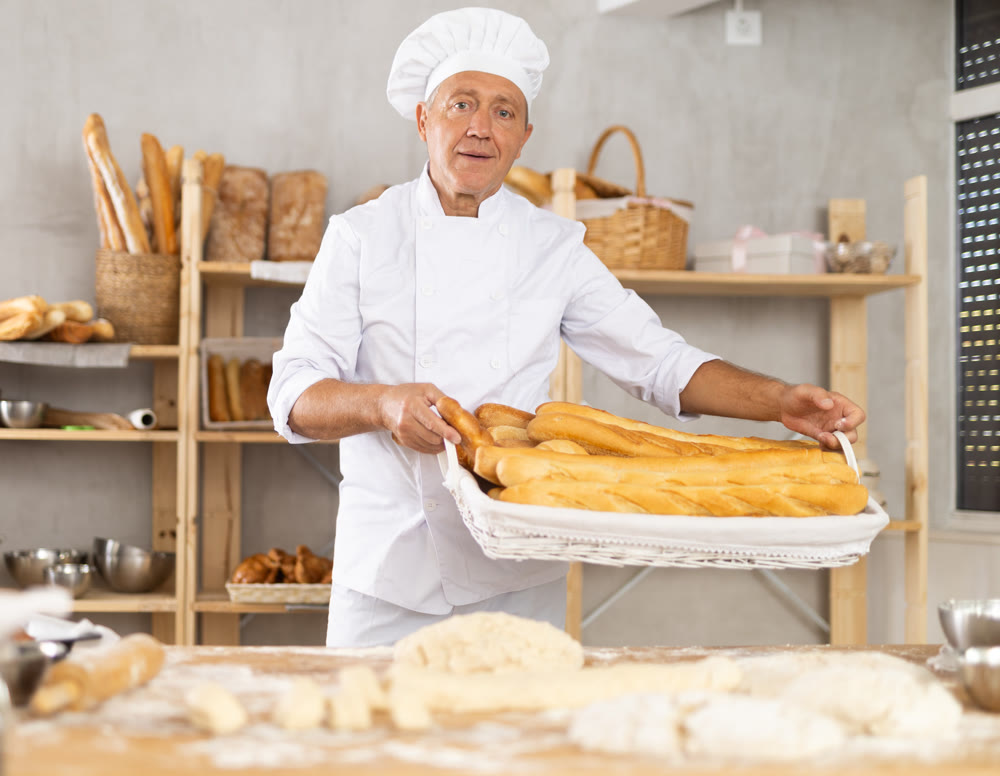 Elderly man baker with basket of baguettes