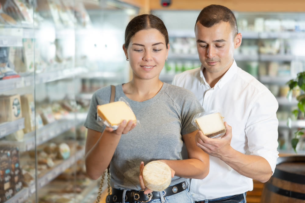 Positive young couple choosing cheese in large supermarket