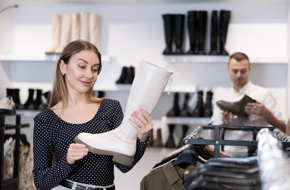 Girl buyer looks at footwear from new collection and picks up new pair of high boot