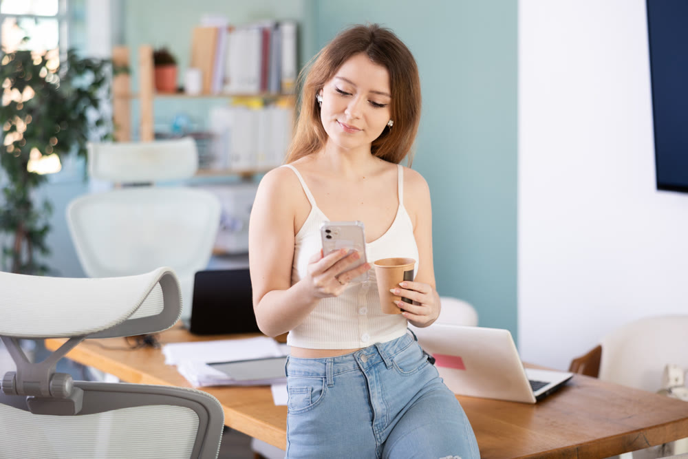 Young woman drinking coffee and scrolling through the feed on smartphone