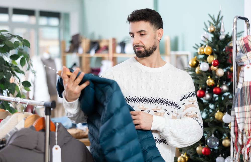 man chooses a down jacket against the background of a Christmas tree in a store