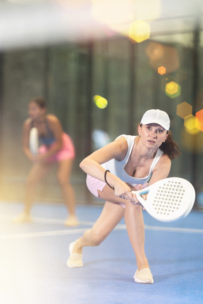 Woman in shorts jumping while playing padel tennis on court. Racket sport training outdoors
