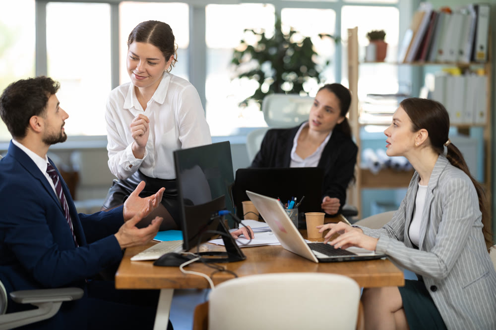 Flirtatious female employee sitting on table and talking to male colleague