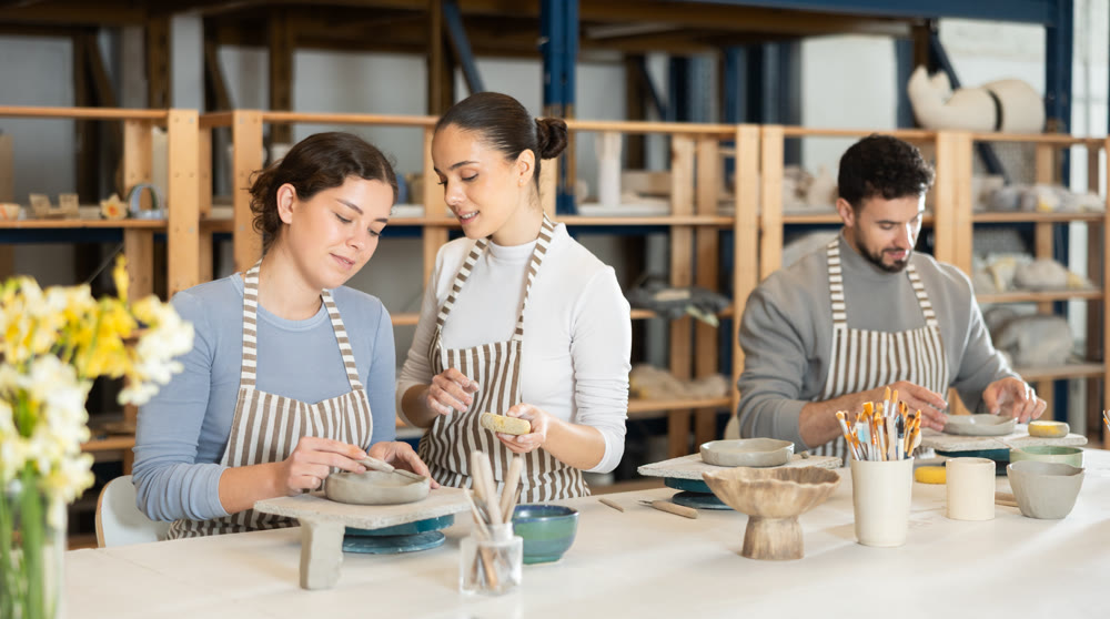 Girl master leaned over to girl and helps to sculpting from clay