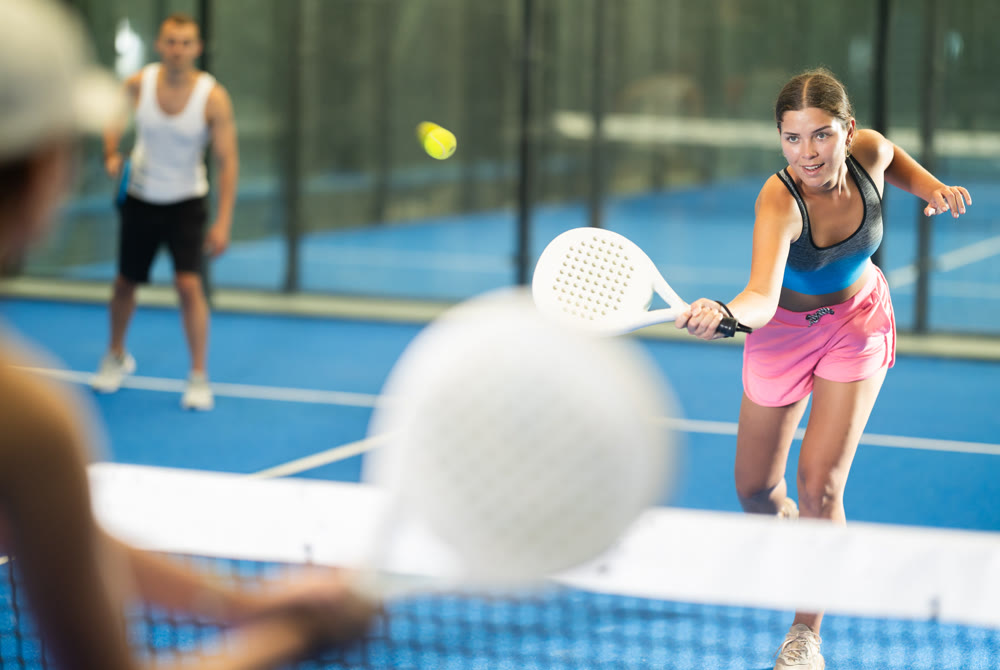 Girl paired with a man plays padel on an indoor tennis court