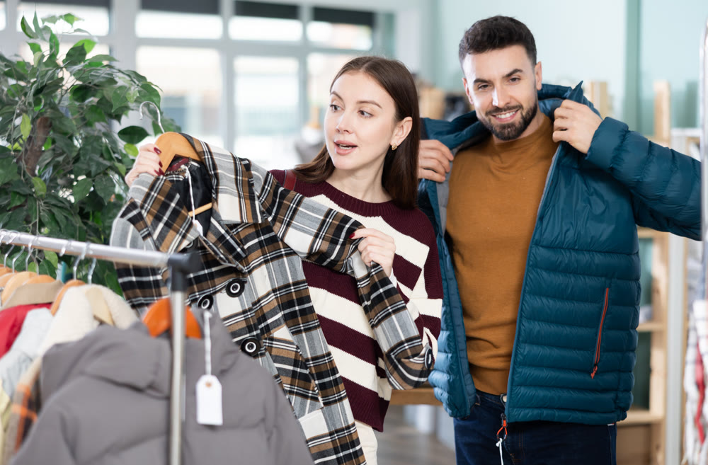 Man try on down jacket, woman elect plaid coat. Family mutual shopping time