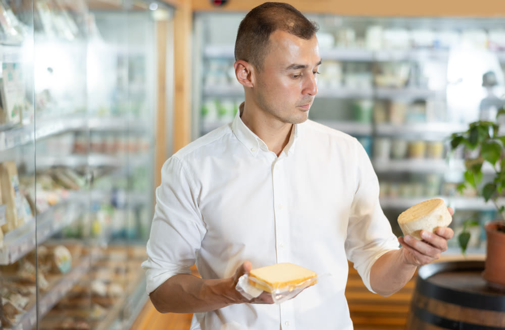 Attentive young man purchaser choosing cheese in large supermarket
