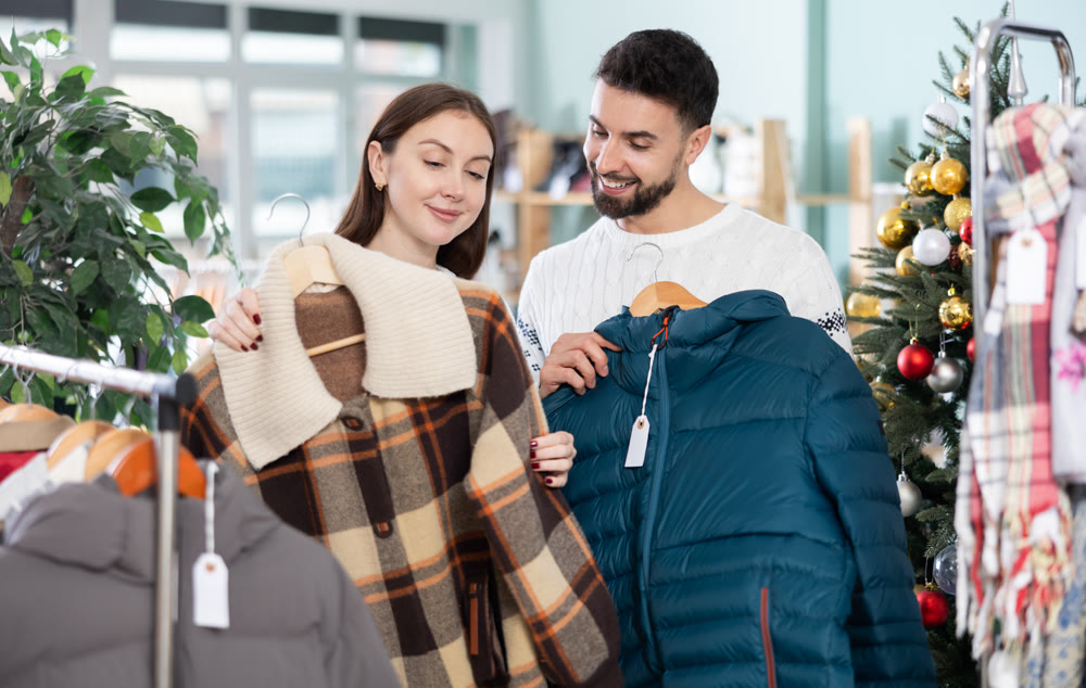Focused woman looking coat for winter season and male salesperson or husband helping with assortment and choice in clothing store