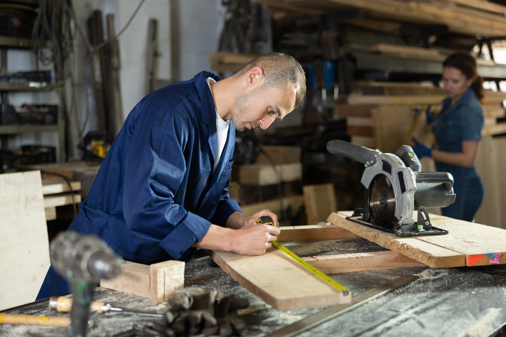 Man employee of carpentry workshop makes measurements of wooden board, counts off set parameters
