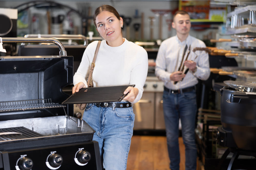 Young woman choosing BBQ grill in store